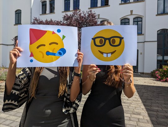 Mitarbeiterinnen mit Emoji-Schildern vorm Gesicht
