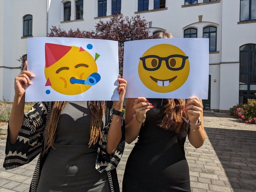 Mitarbeiterinnen mit Emoji-Schildern vorm Gesicht