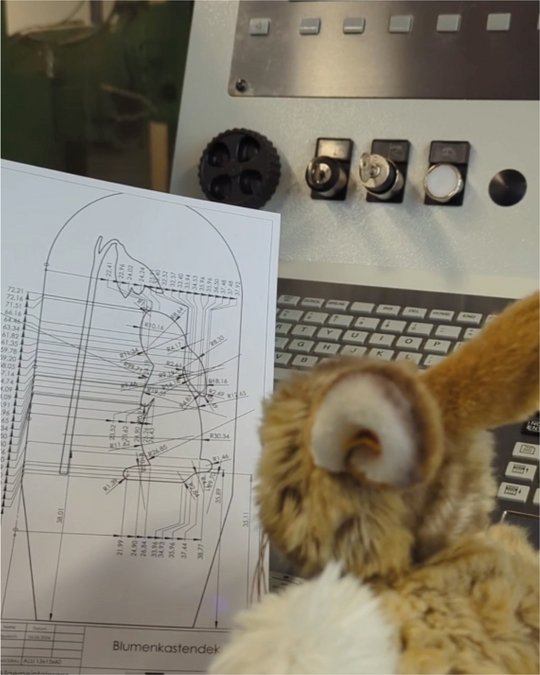 Osterhase sitzt mit Skizze vor CNC-Maschine